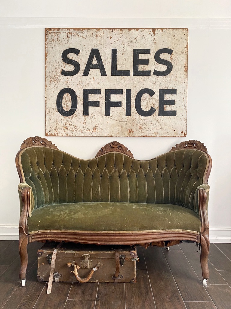 A green velvet settee under a vintage sales office sign